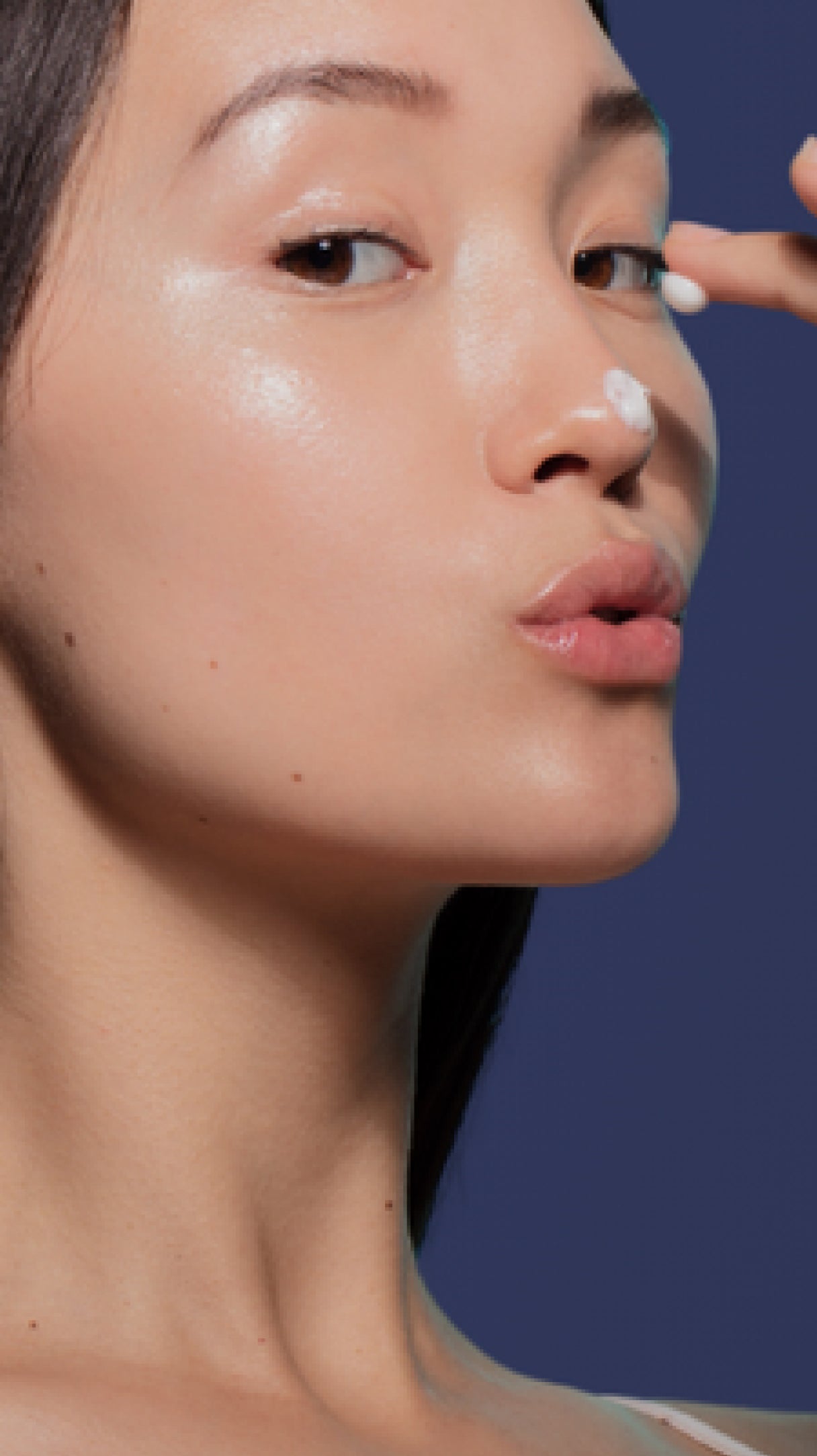 Close-up of a person applying cream to their face with a blue background